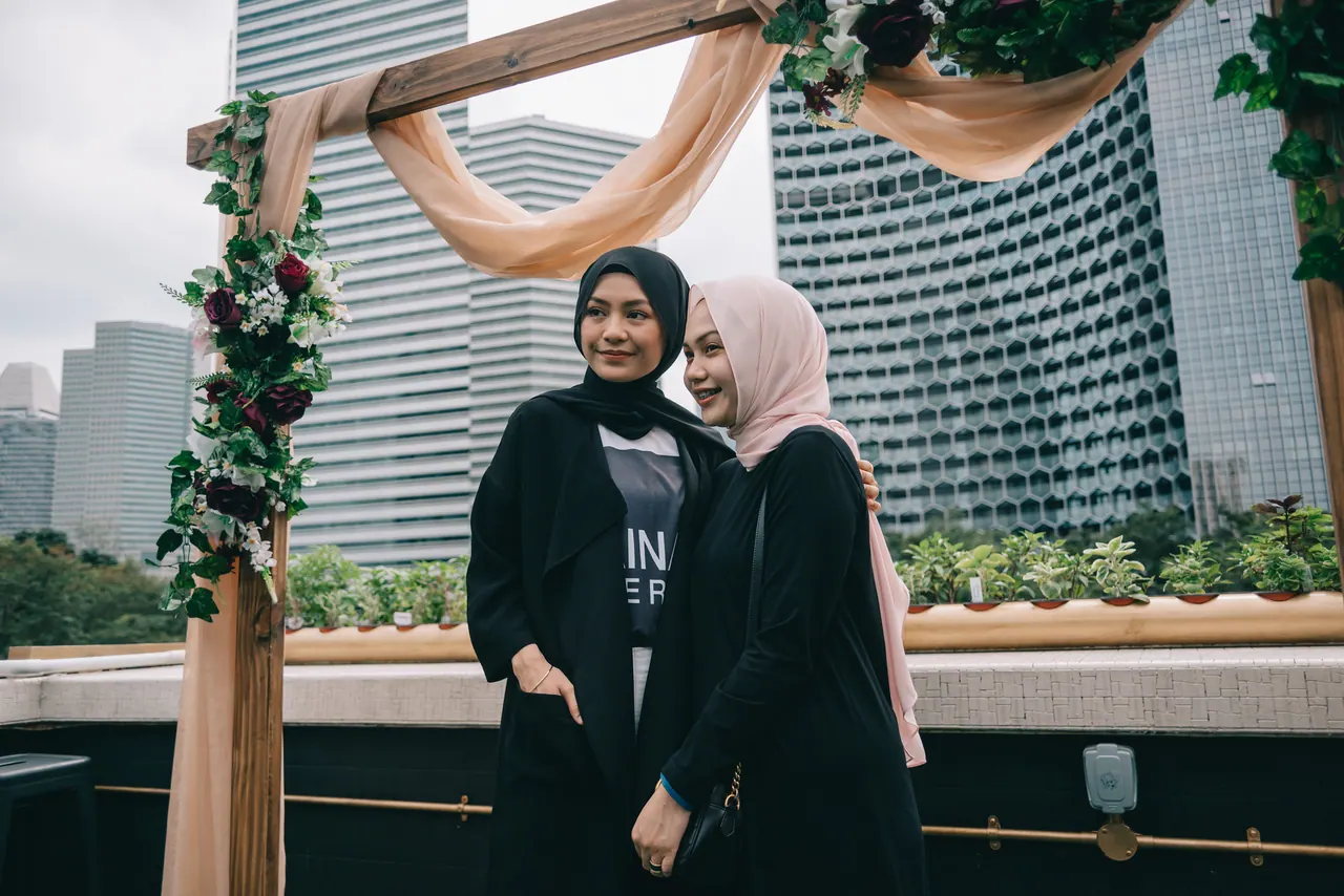Two women chat under a floral arch on the rooftop.