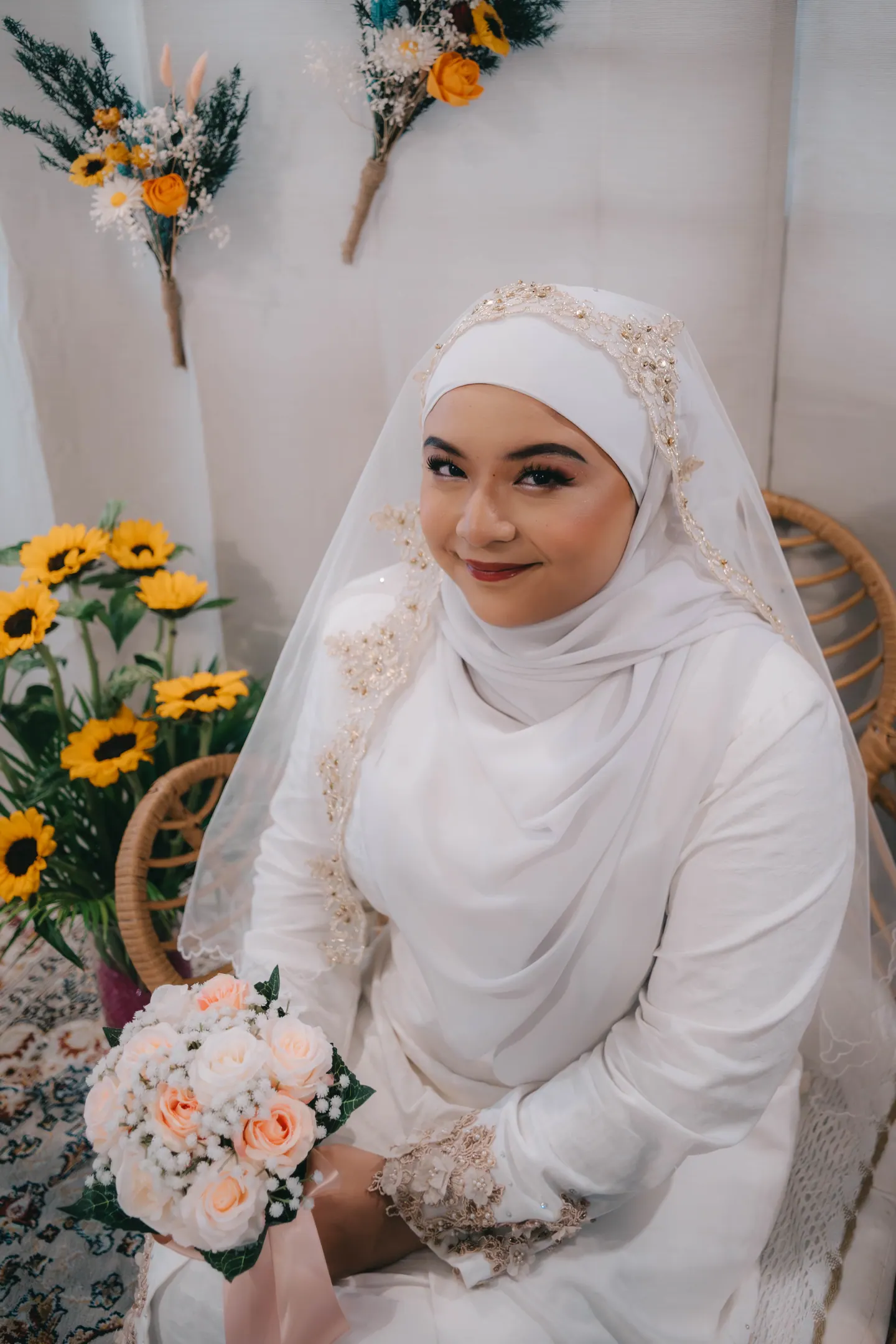 The bride-to-be in white, seated beside sunflowers, smiles at the camera.