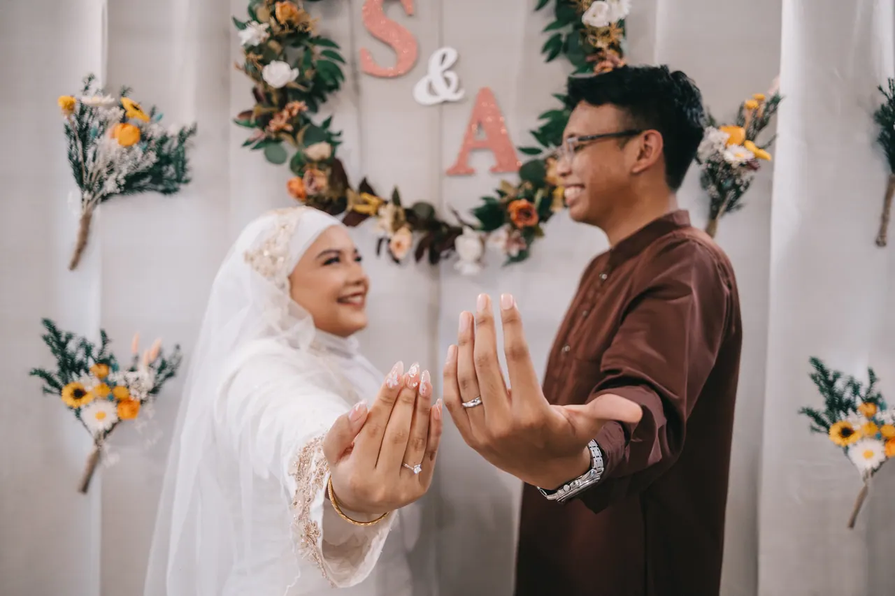 The couple hold out their hands to show their rings, laughing.