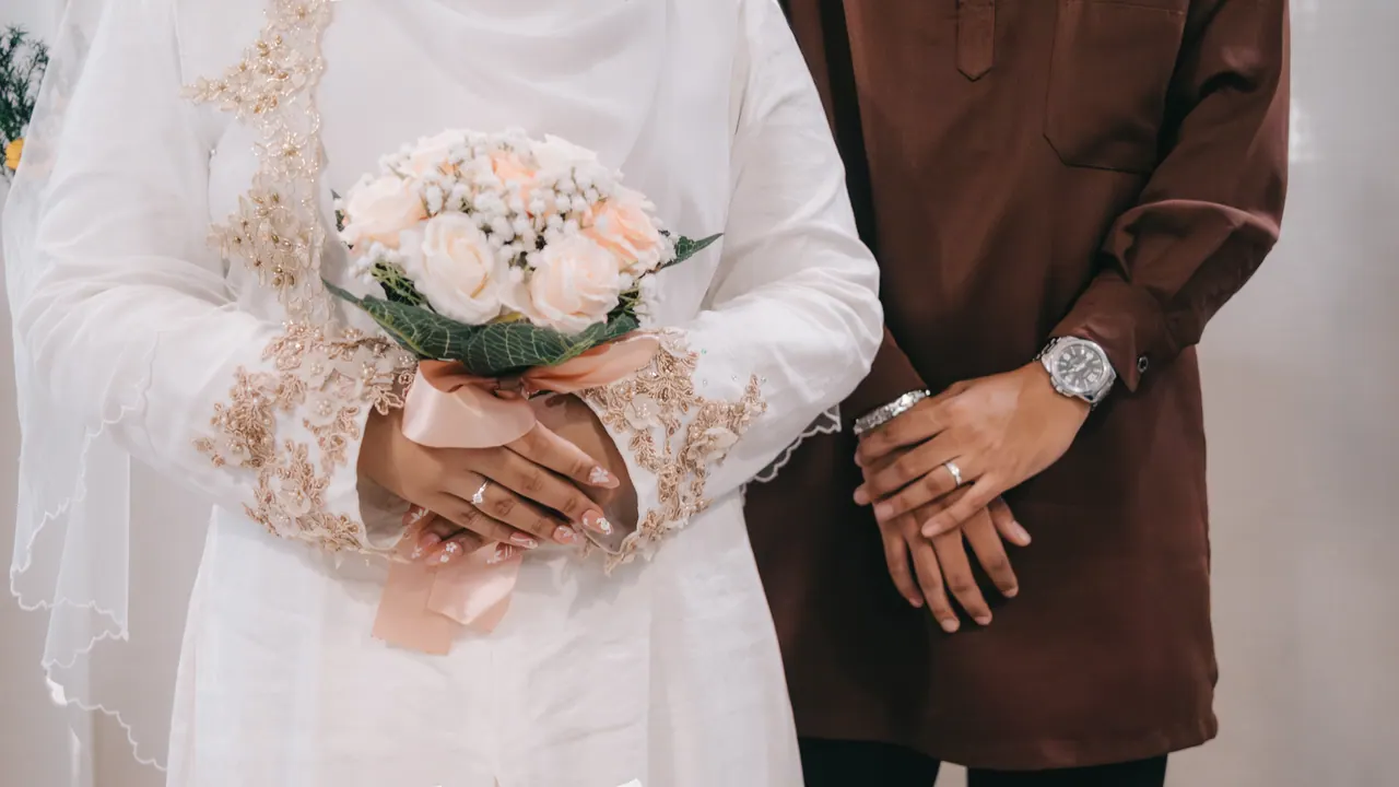 Their hands side by side: hers on a bouquet, his at his wrist.