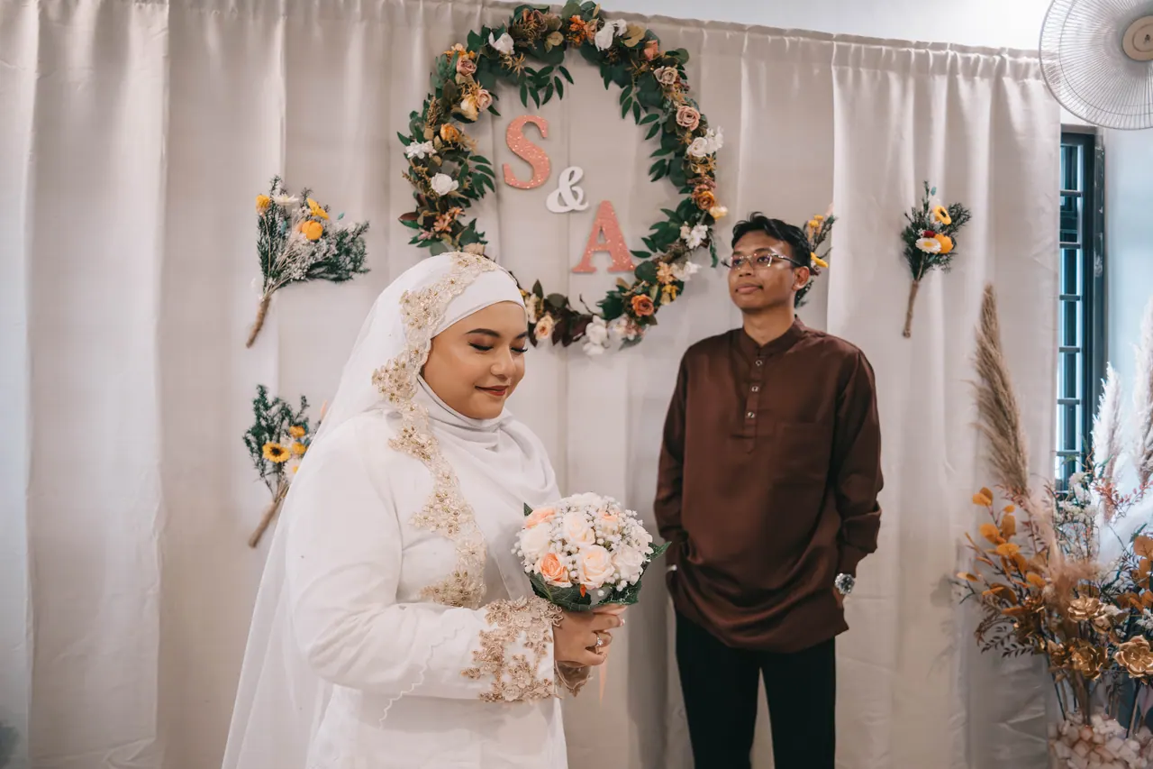 The couple stand apart in front of the S & A wreath.