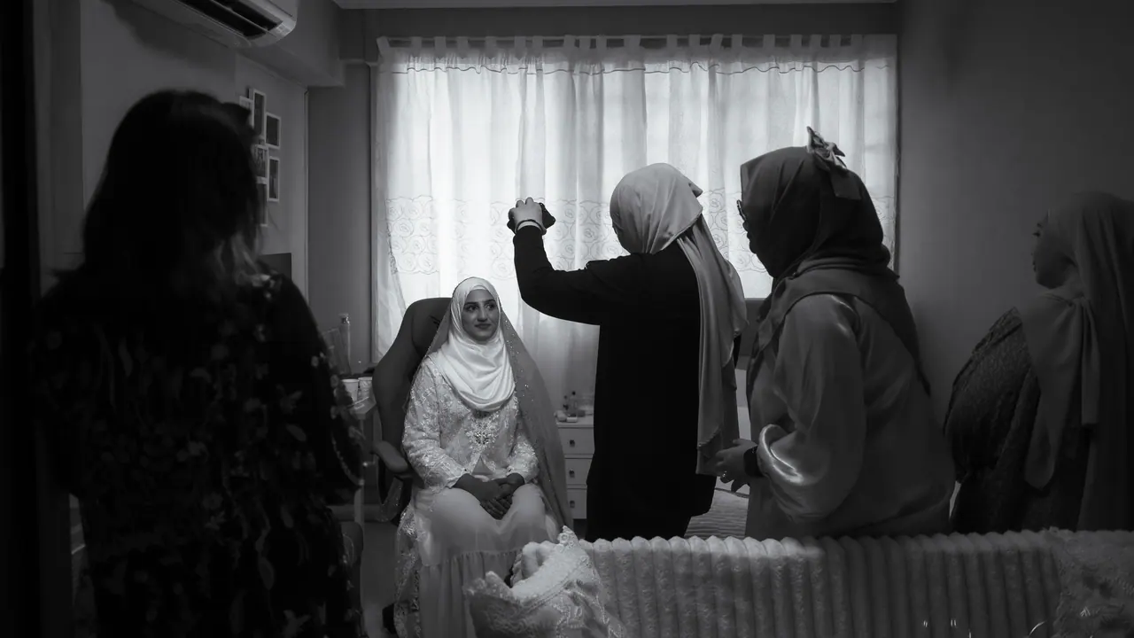 Black and white: women gather around the bride-to-be in a bedroom, seen from the doorway.