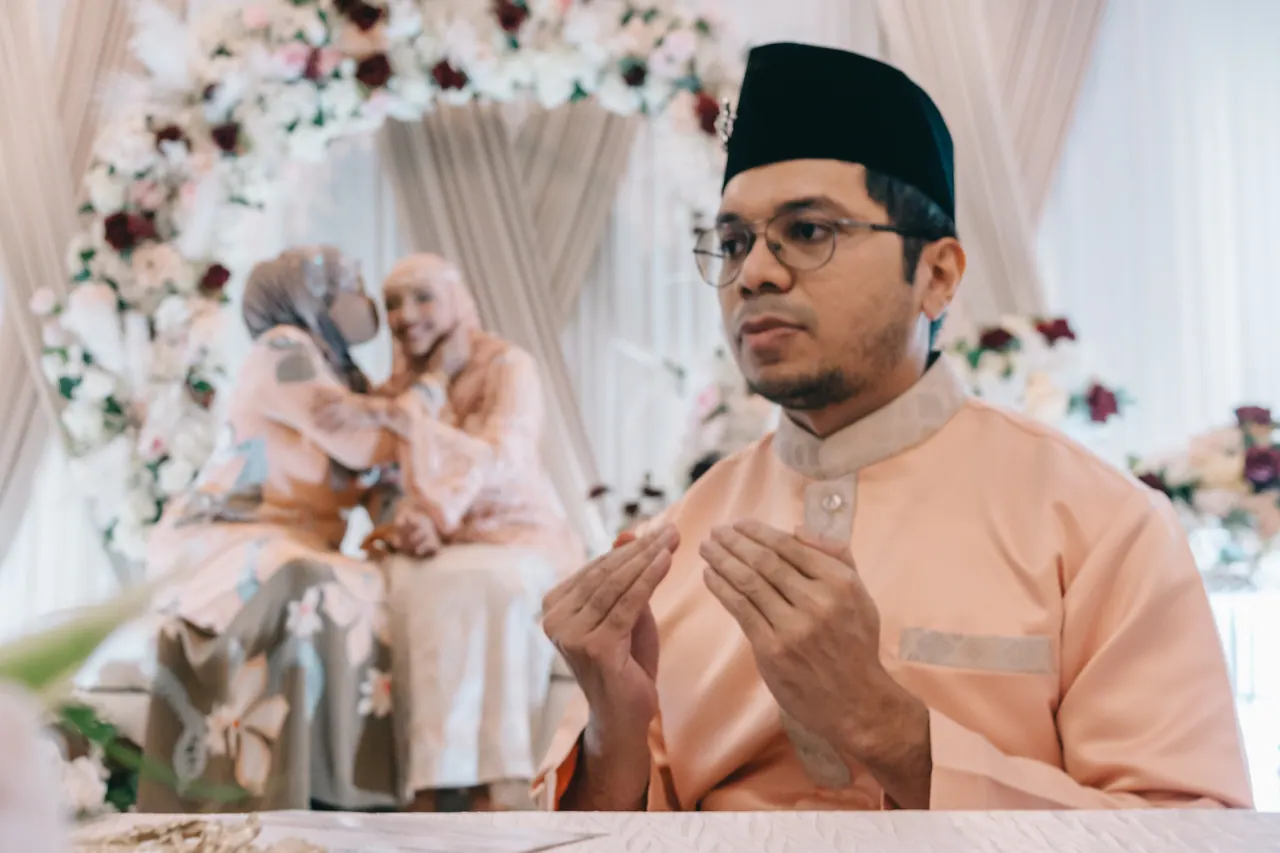 The groom raises his hands in prayer while two women embrace behind him.