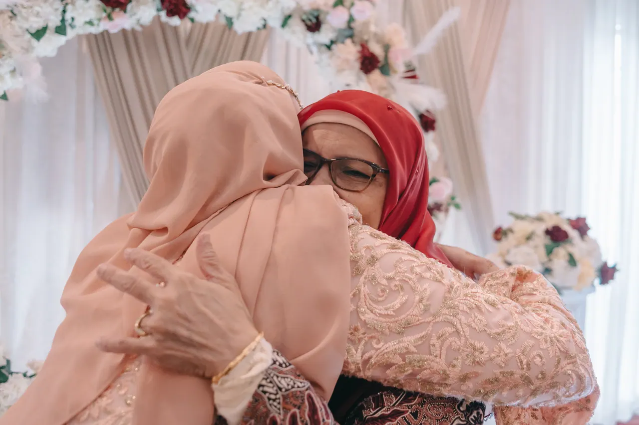 Two women hold each other in a long embrace in front of a floral arch.