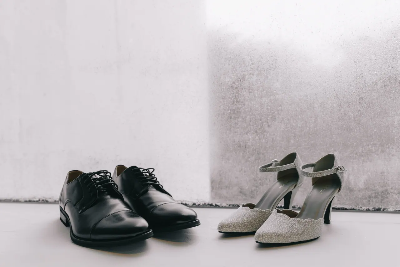 Black leather shoes and glittering heels against a concrete wall.