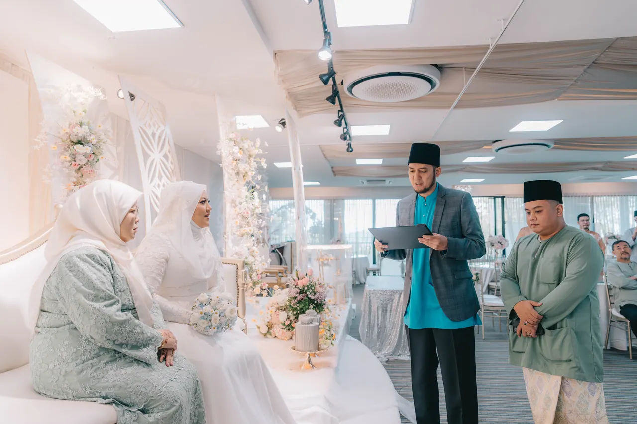 An official reads from a folder as the bride and an older woman sit on a white sofa.