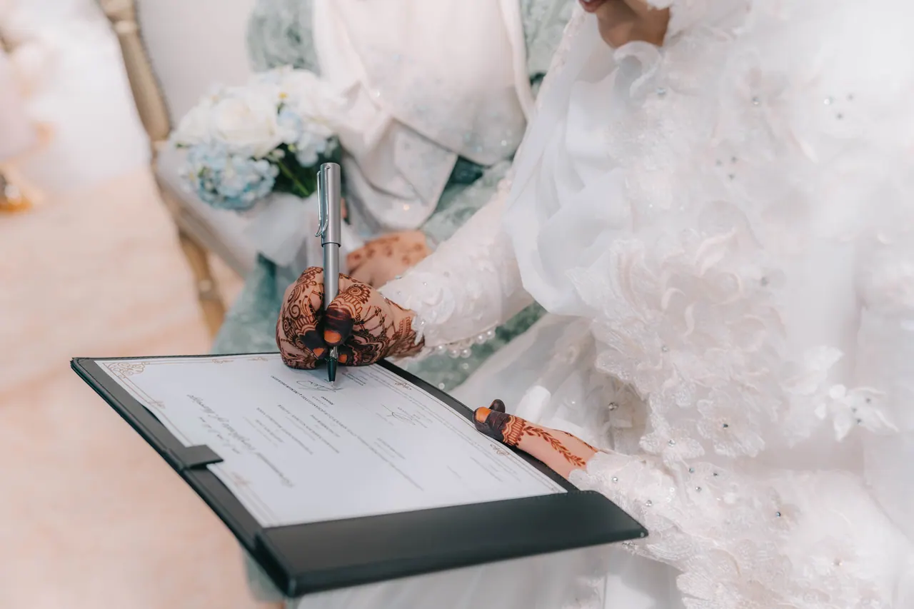 The bride, her hands painted with henna, signs the certificate.