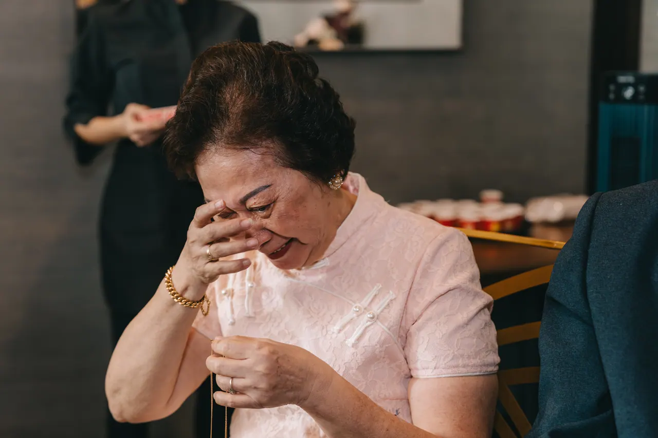 An older woman in pink wipes her eyes during the tea ceremony.