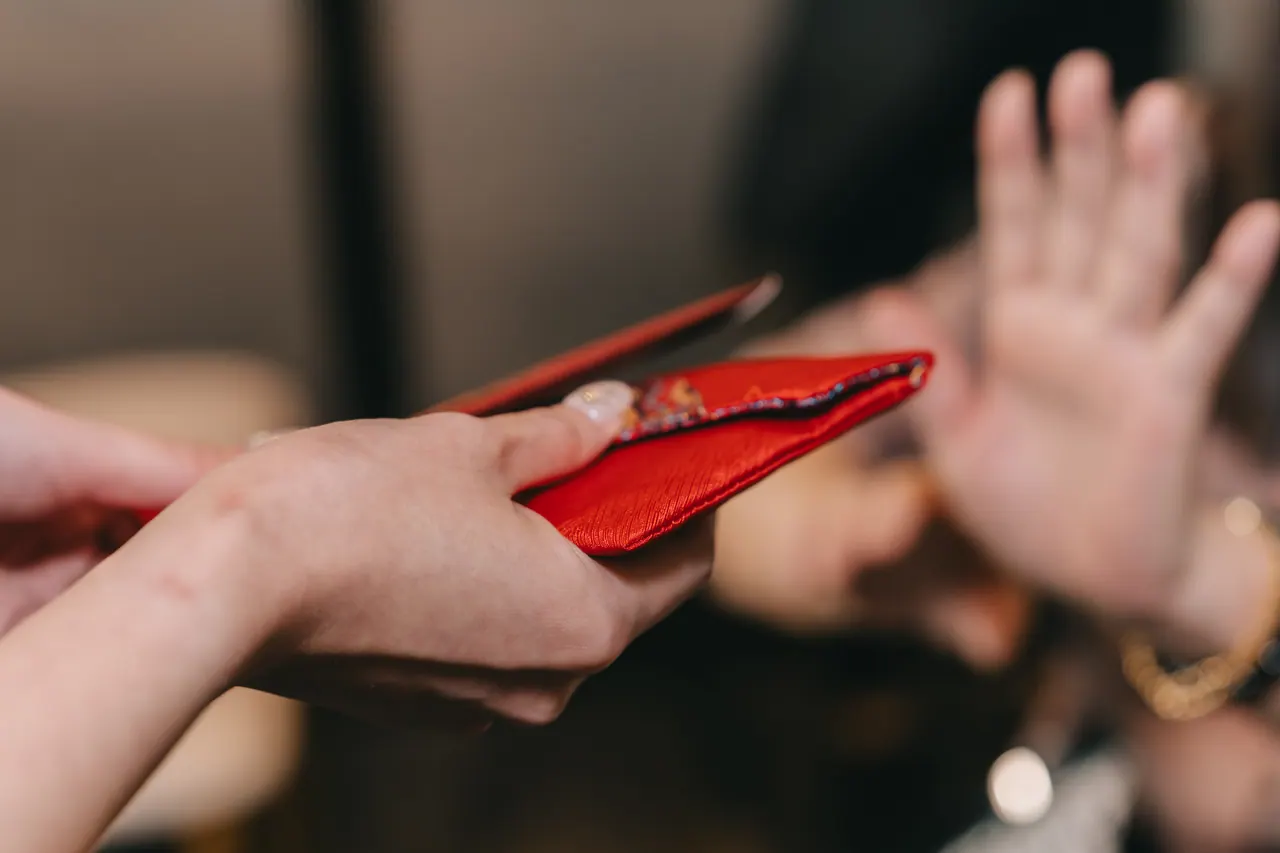 A red packet held out; a hand raised in front of it.