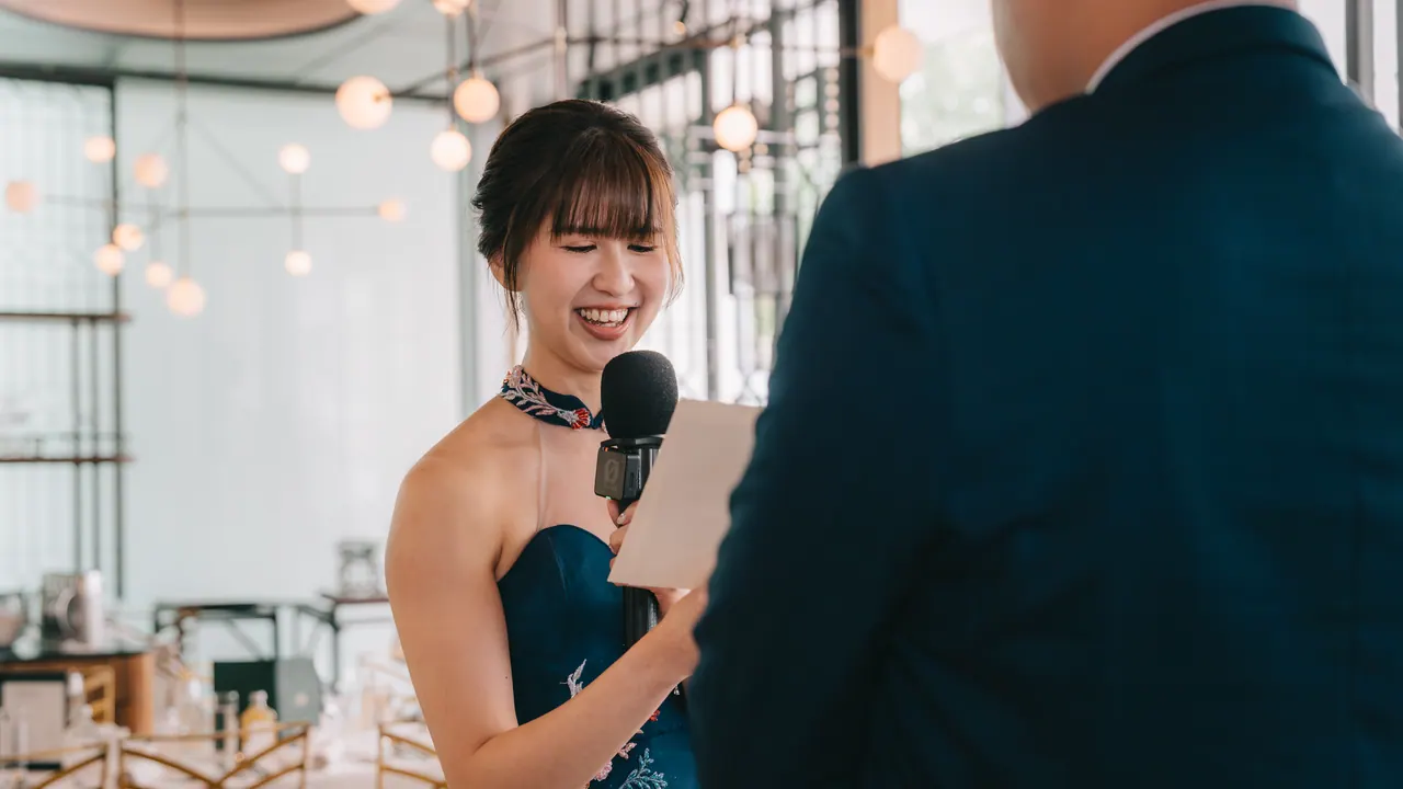 The bride laughs as she reads her vows into a microphone.