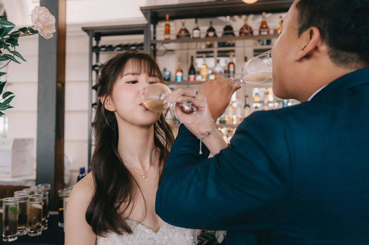 The bride sips champagne beside the groom.