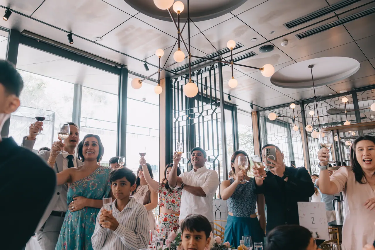 Guests stand with glasses raised under globe lights.