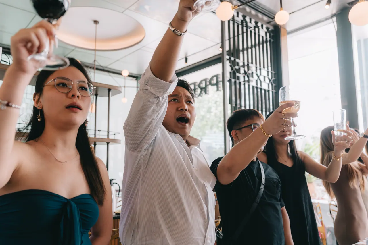 Guests shout with their glasses held overhead.