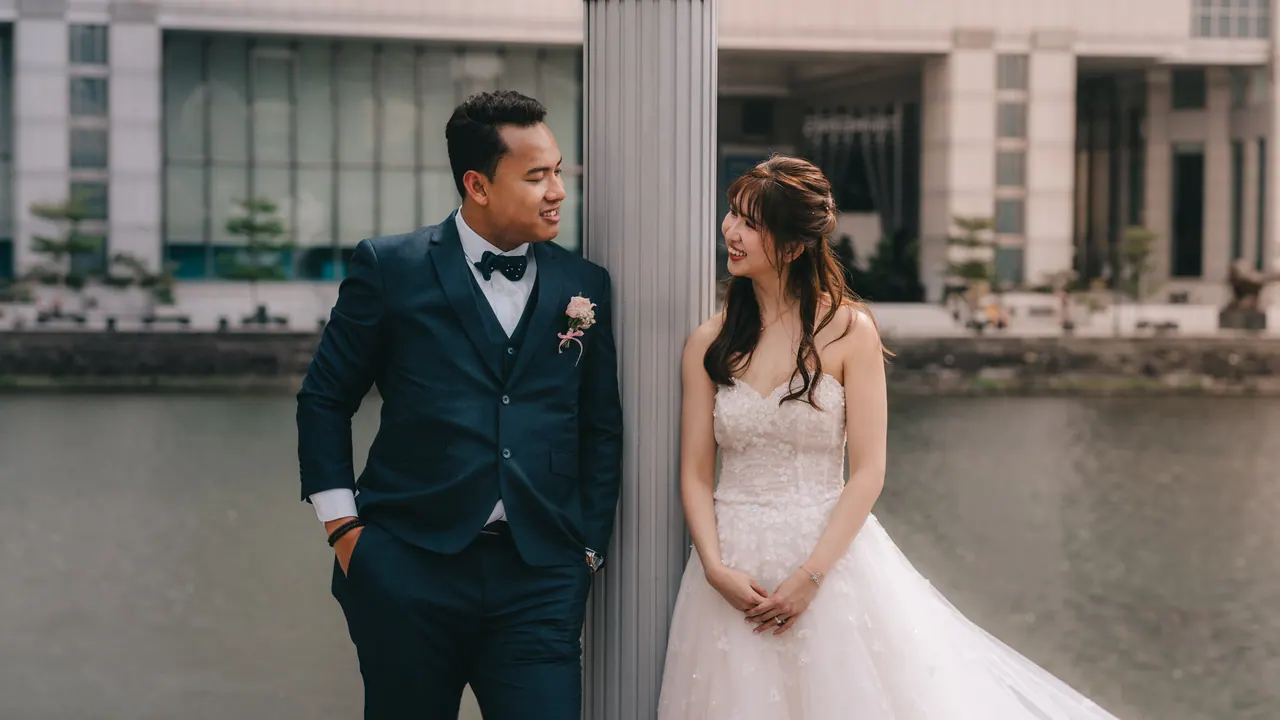 Bride and groom on either side of a pillar by the river.