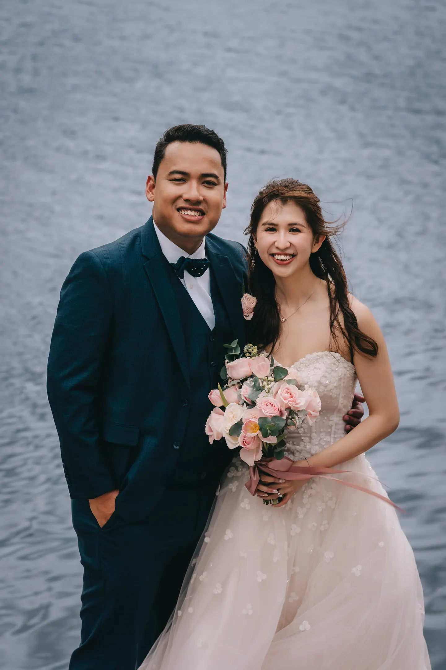 Bride and groom smile together, the water behind them.