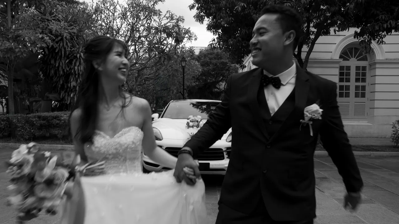Black and white: the couple walk hand in hand, laughing.