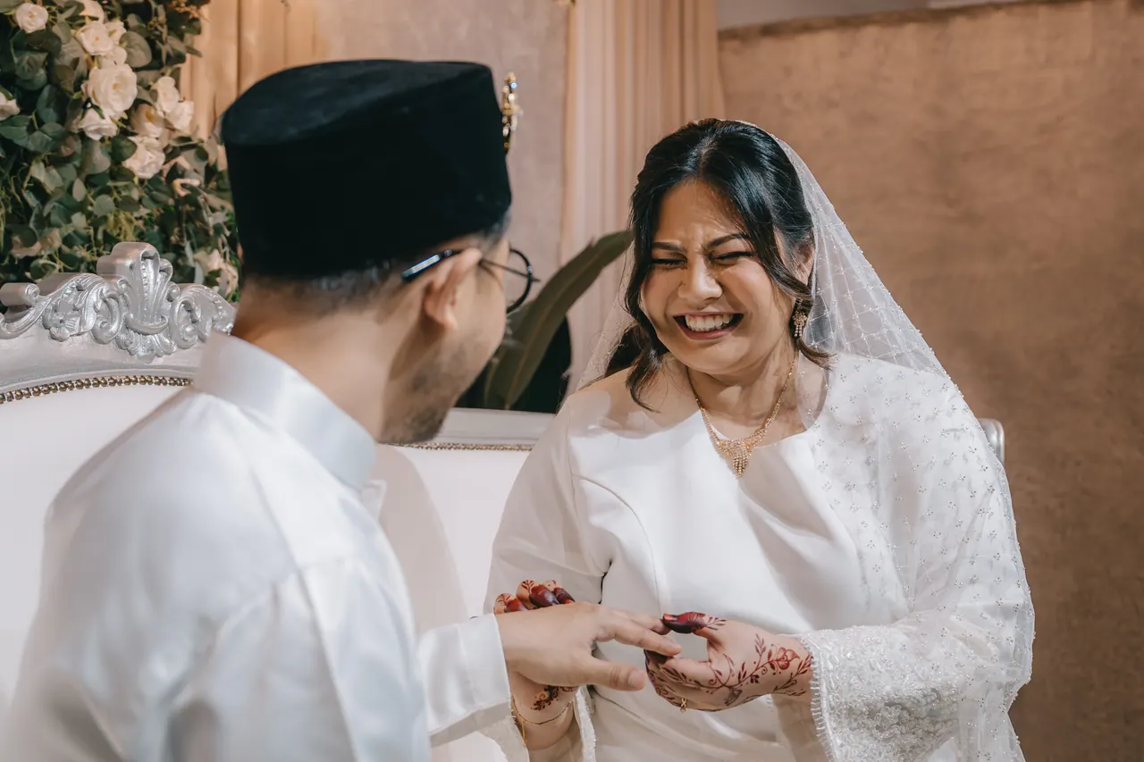 The groom slides a ring onto the bride’s hennaed finger and she laughs.