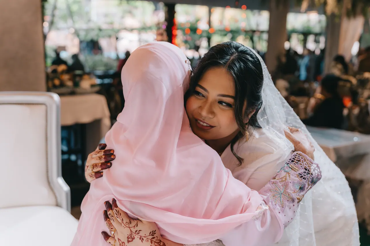 A woman in a pink headscarf hugs the bride tightly.