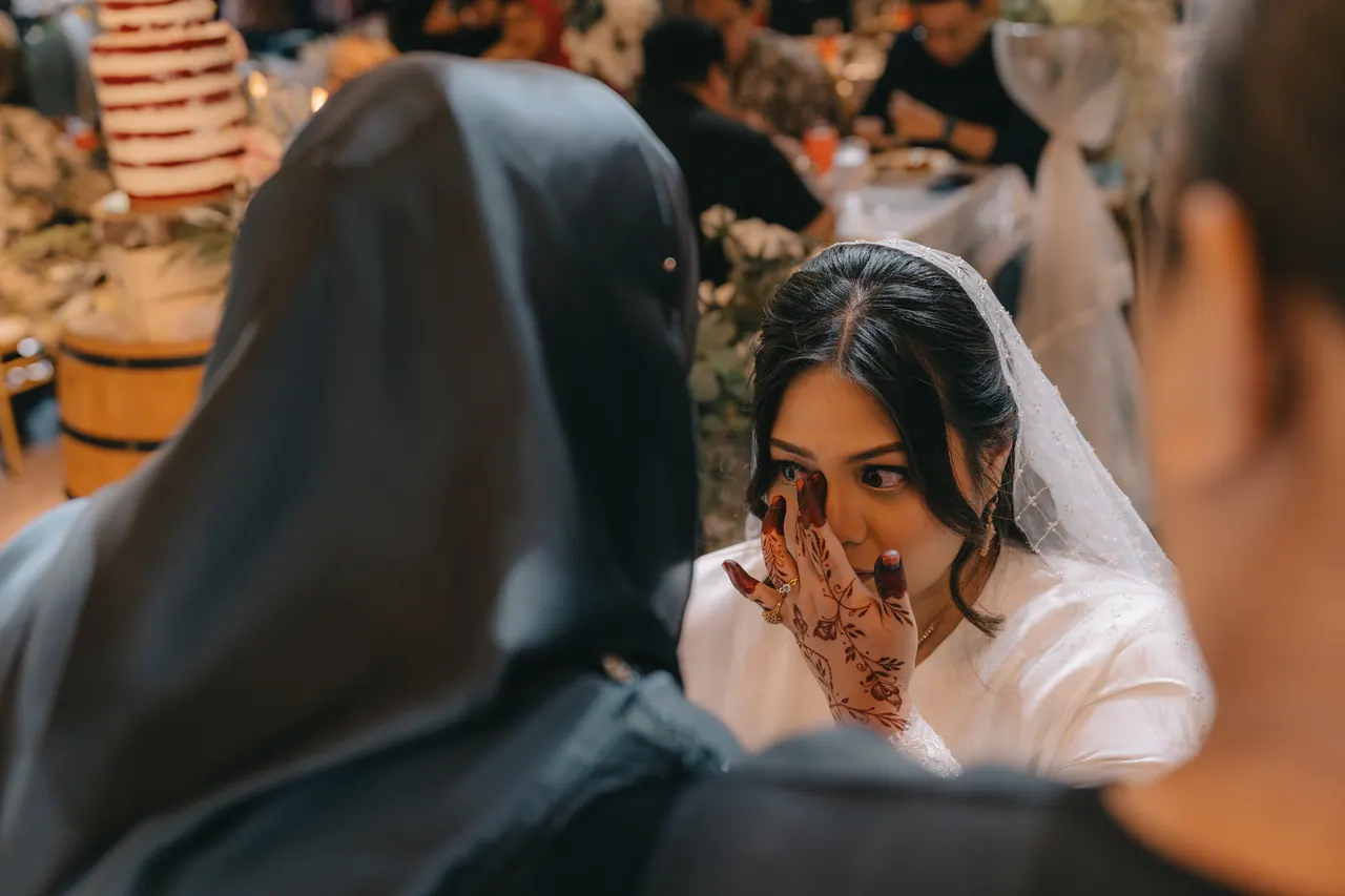 The bride wipes away a tear, framed by two guests.