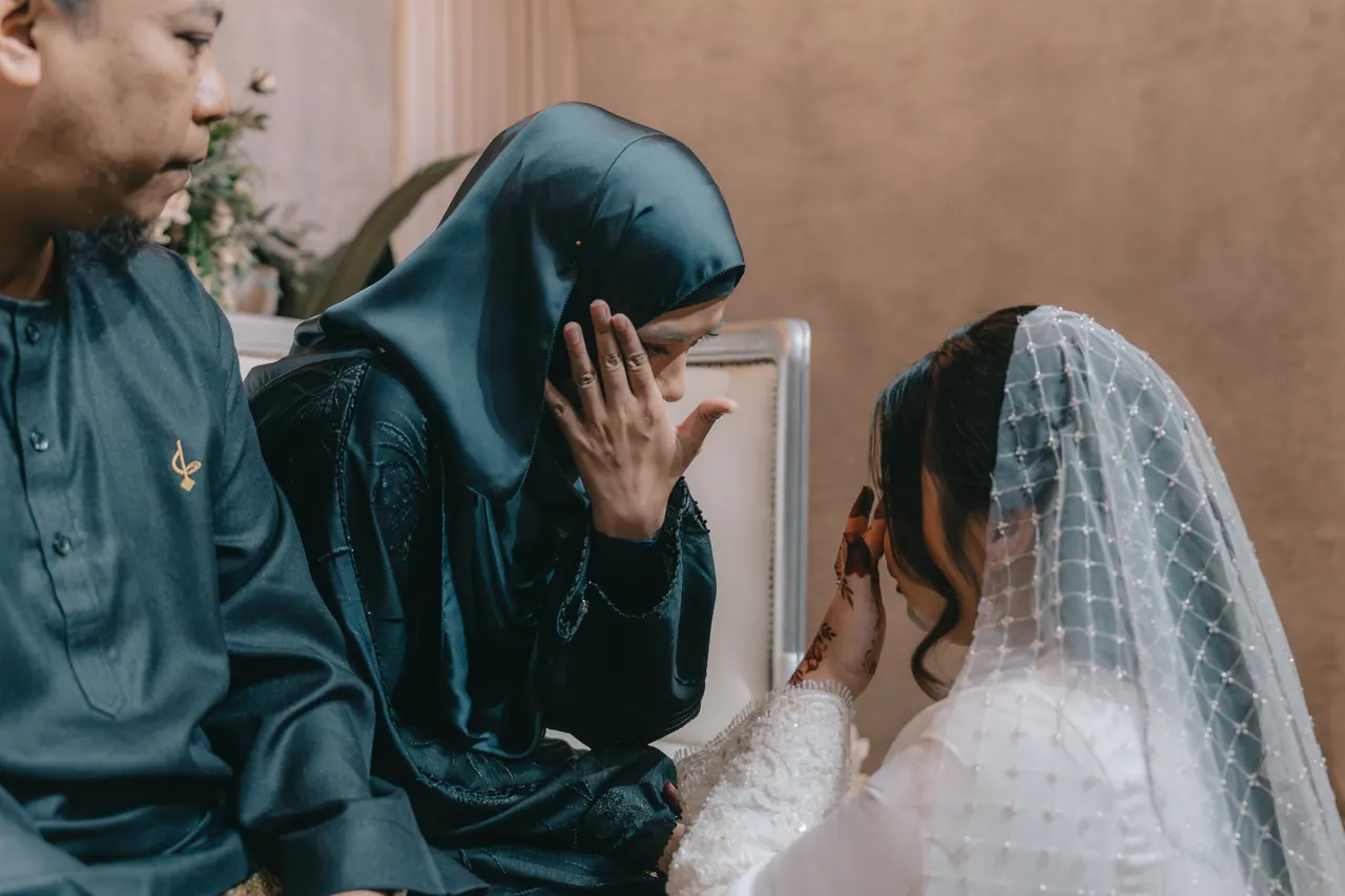 A woman reaches out to wipe the bride’s tears while a man watches.