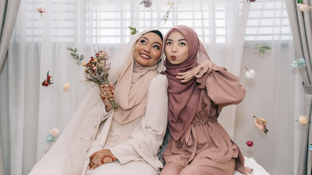 The bride-to-be and a friend pose under hanging flowers.