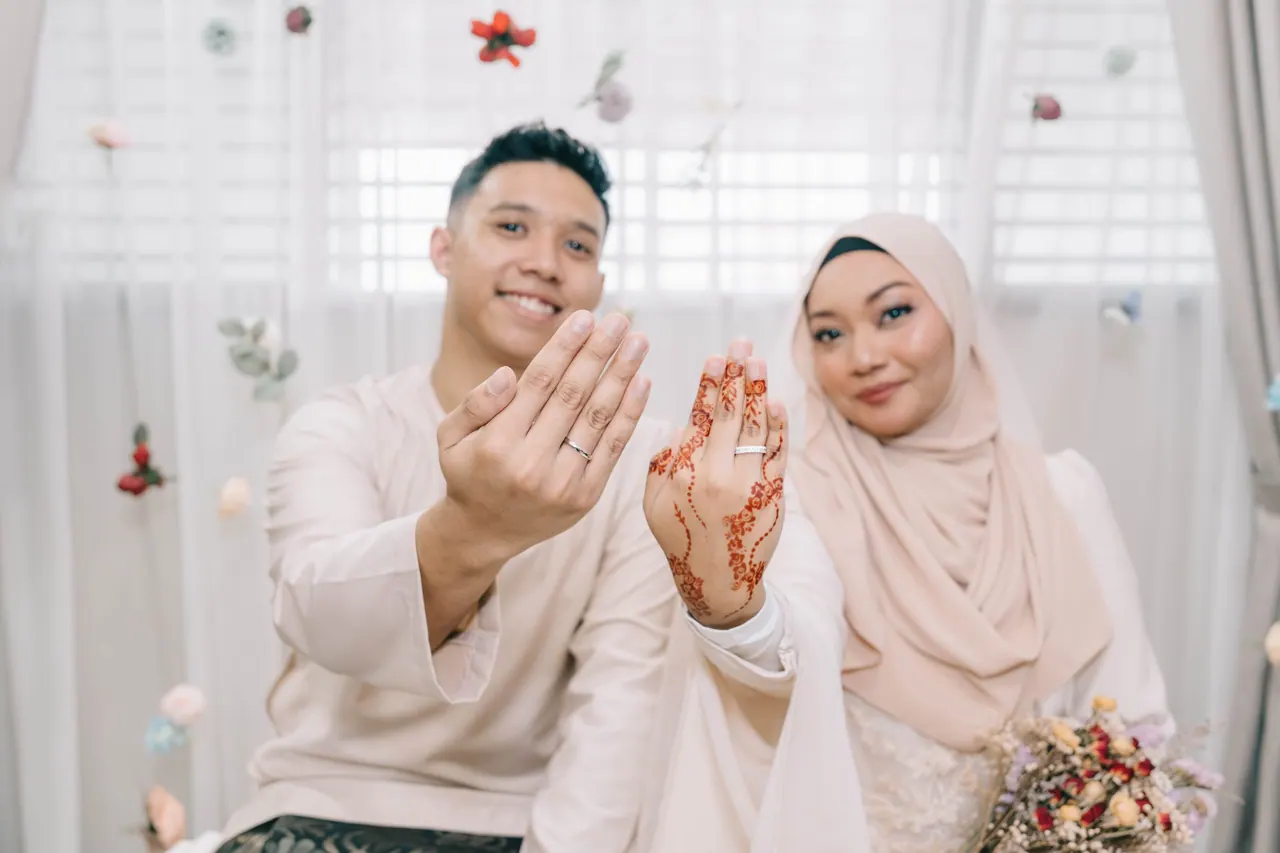 The couple hold up their hands, hers painted with henna, to show the rings.