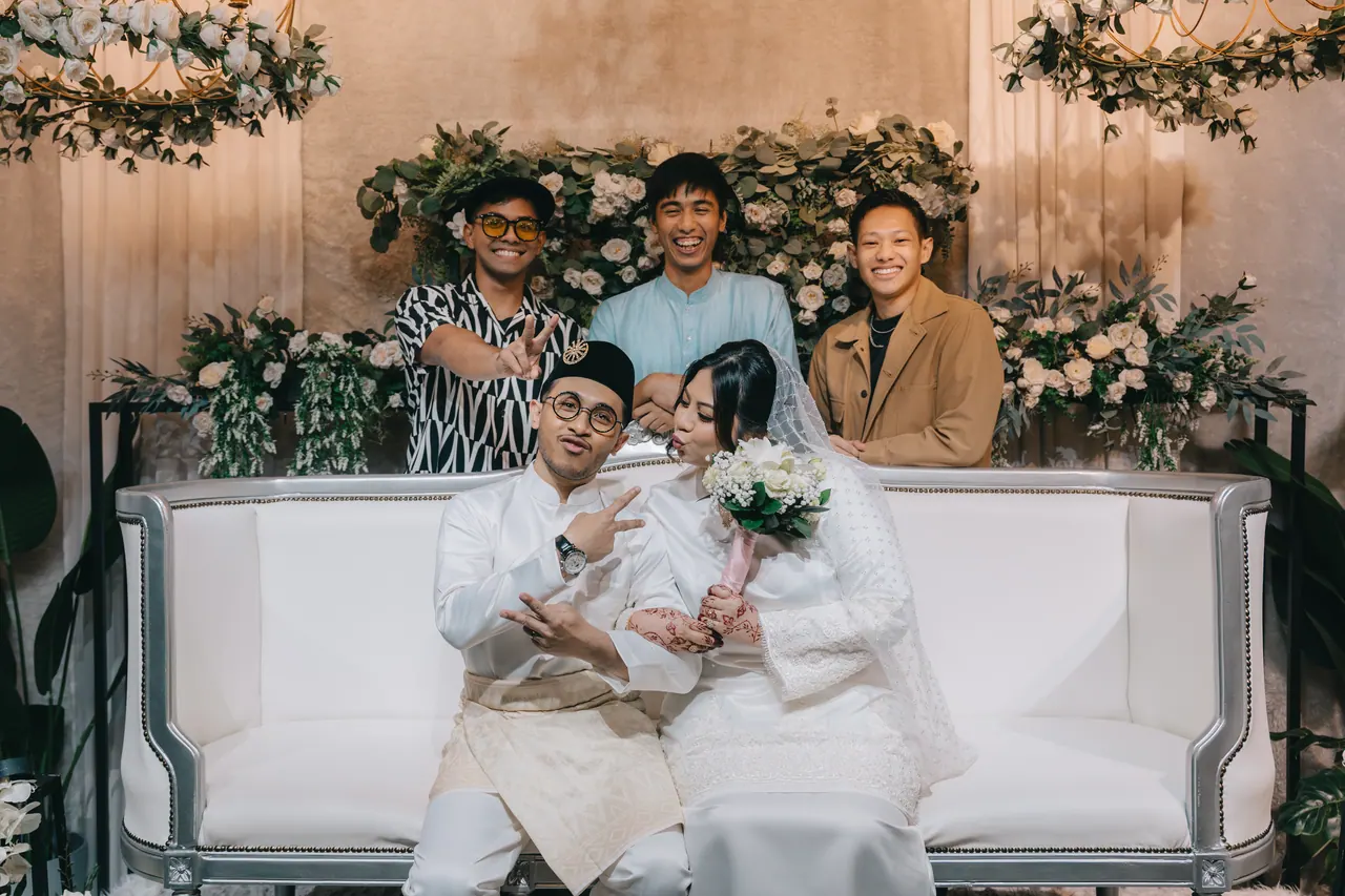 Friends lean over the sofa behind the seated couple, everyone pulling a face.
