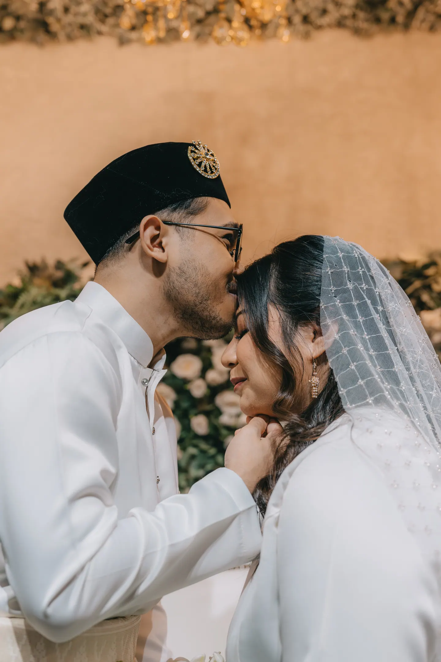 The groom kisses the bride’s forehead; her eyes are closed.