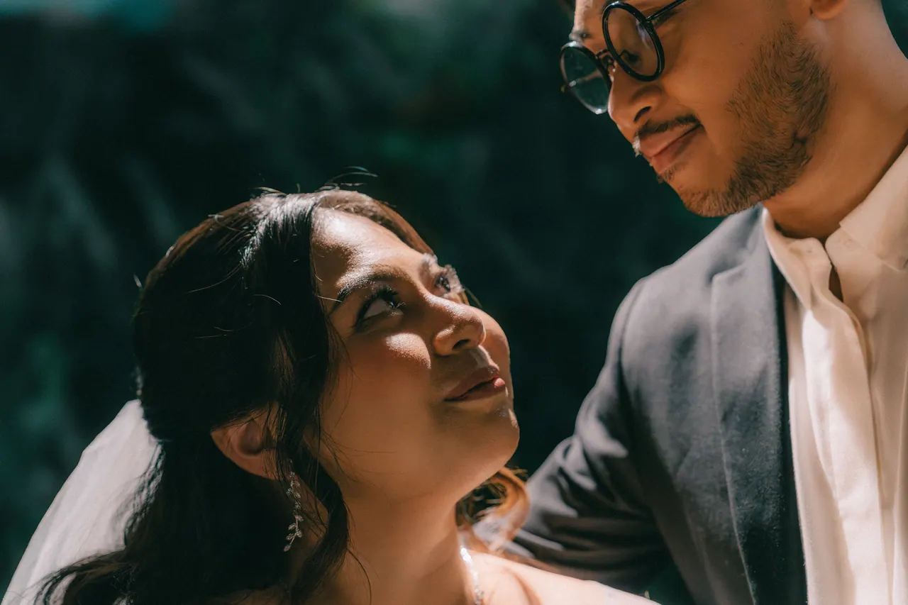 At night, the bride looks up at the groom, light falling across her face.