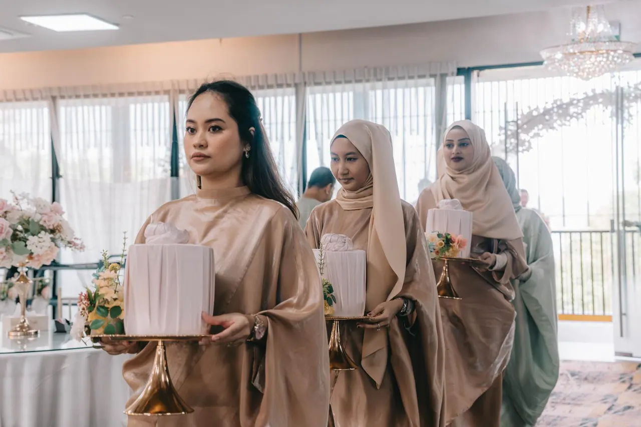 Bridesmaids in dusty rose carry wrapped gifts on gold stands through the room.