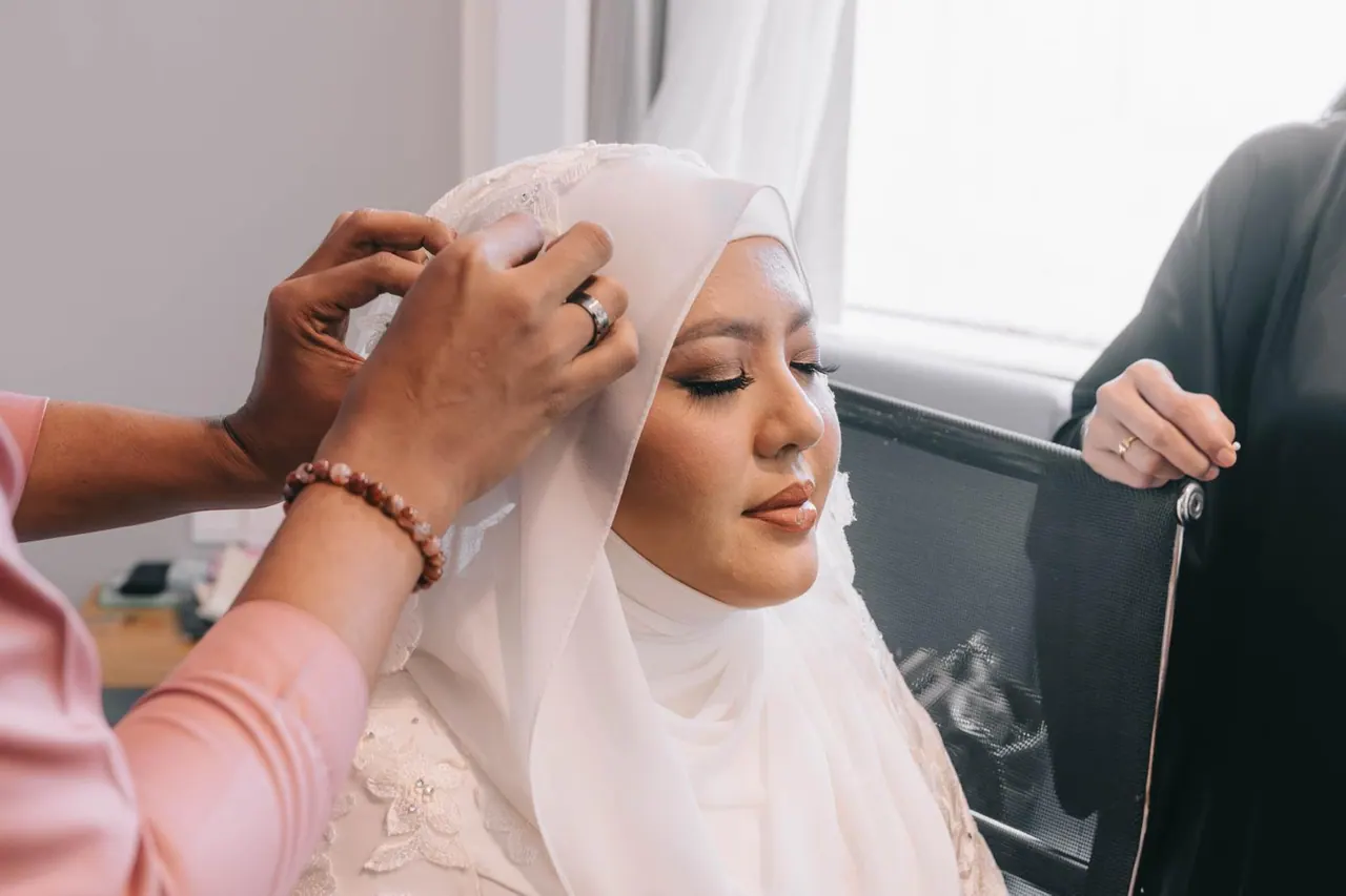 Hands pin the bride's white veil into place as she looks ahead.