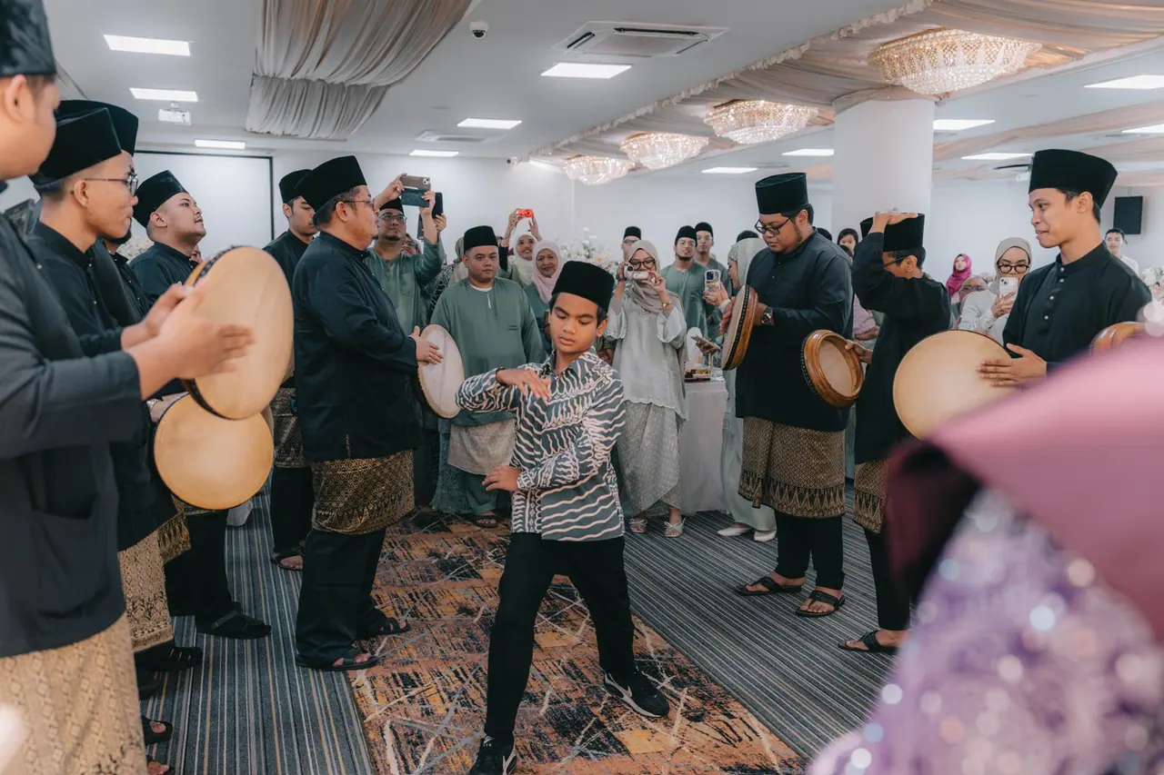 Kompang players with hand drums line the aisle while a boy dances in the middle.