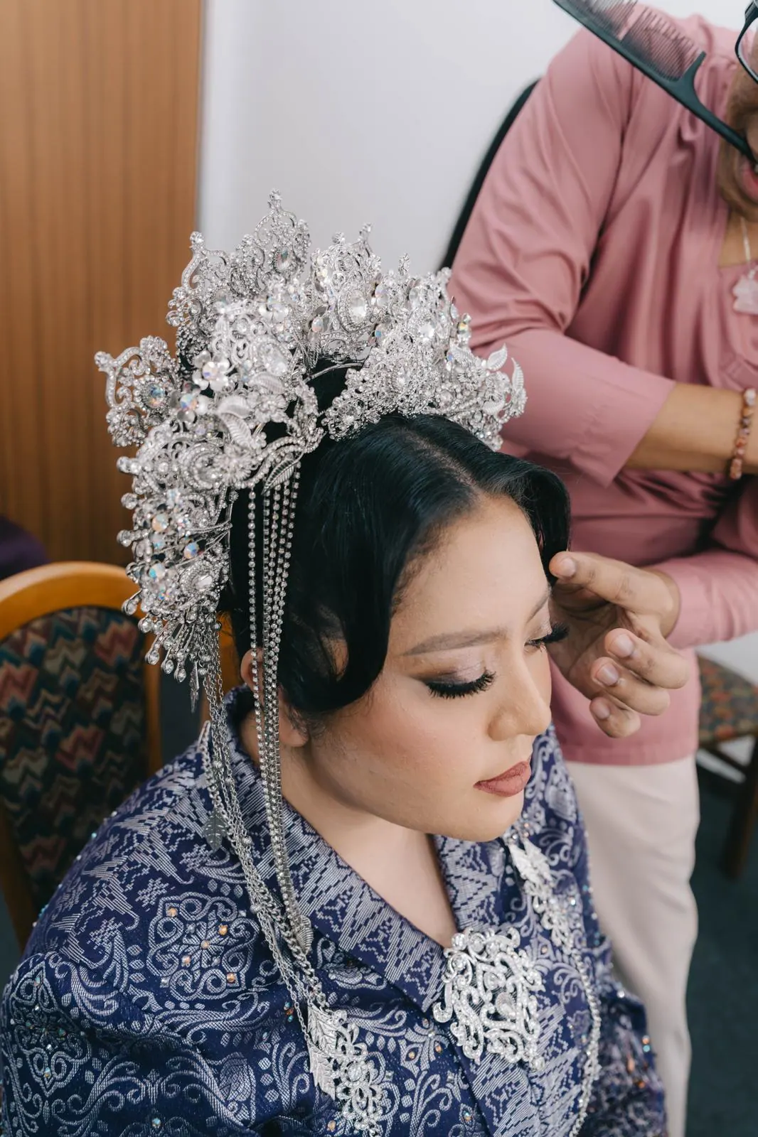 The bride in a purple and silver outfit and tall silver headpiece, eyes lowered.