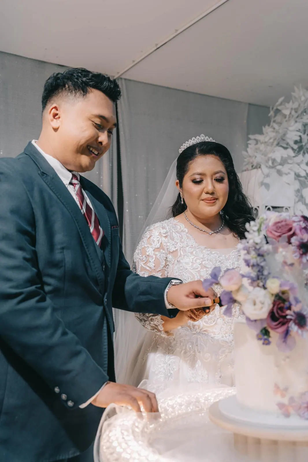 Bride and groom cut a white cake decorated with lilac flowers.