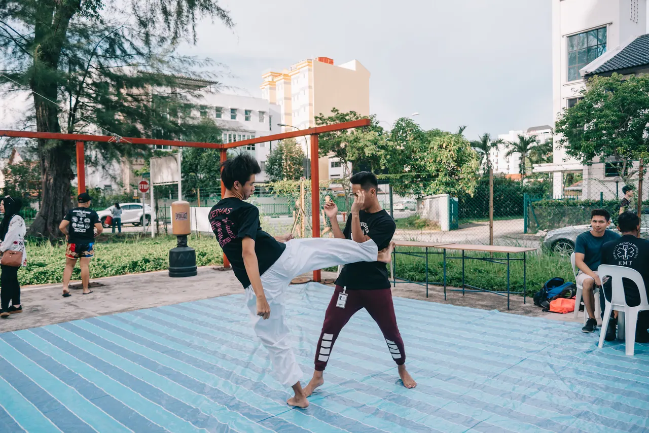 Two fighters warm up on a blue mat outdoors.
