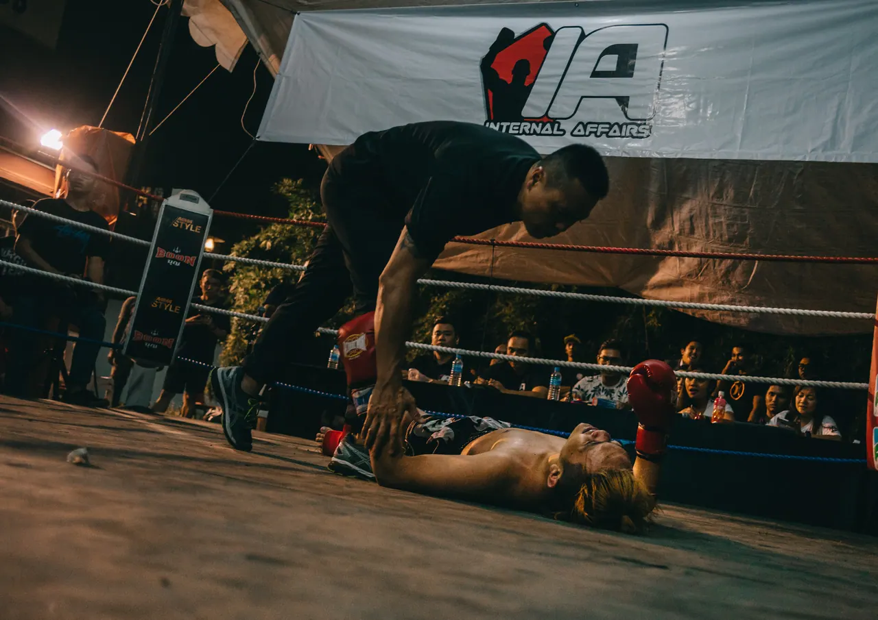 The referee checks on a fighter on the canvas.