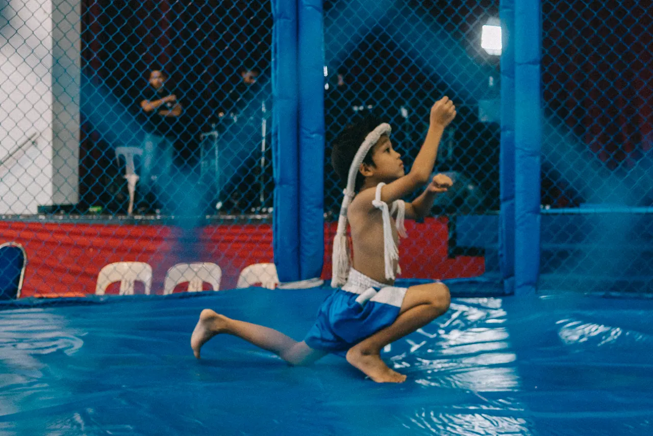 A fighter kneels on the mat, looking up, inside the cage.