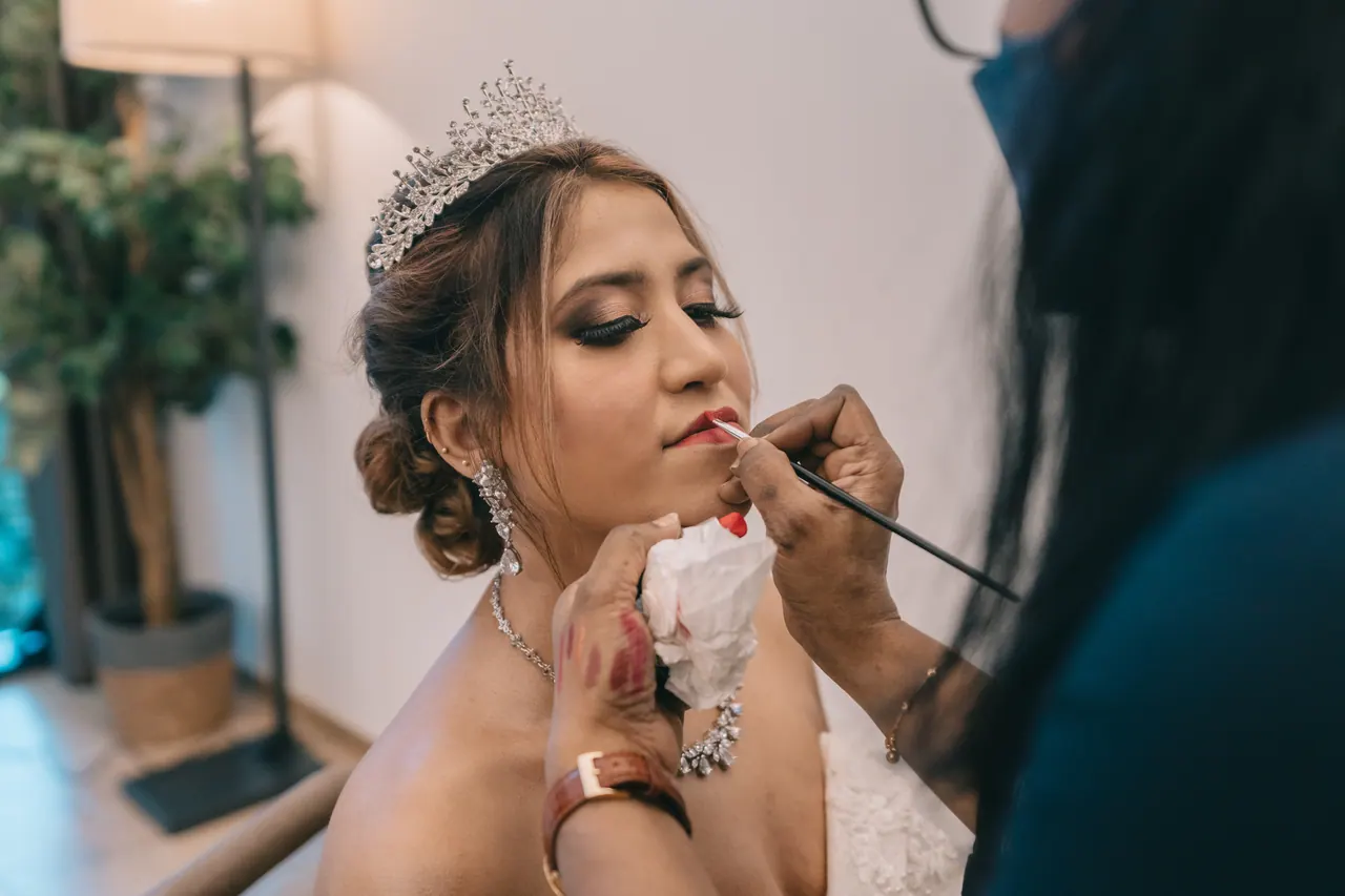 The bride, in a tiara, has her lipstick applied.