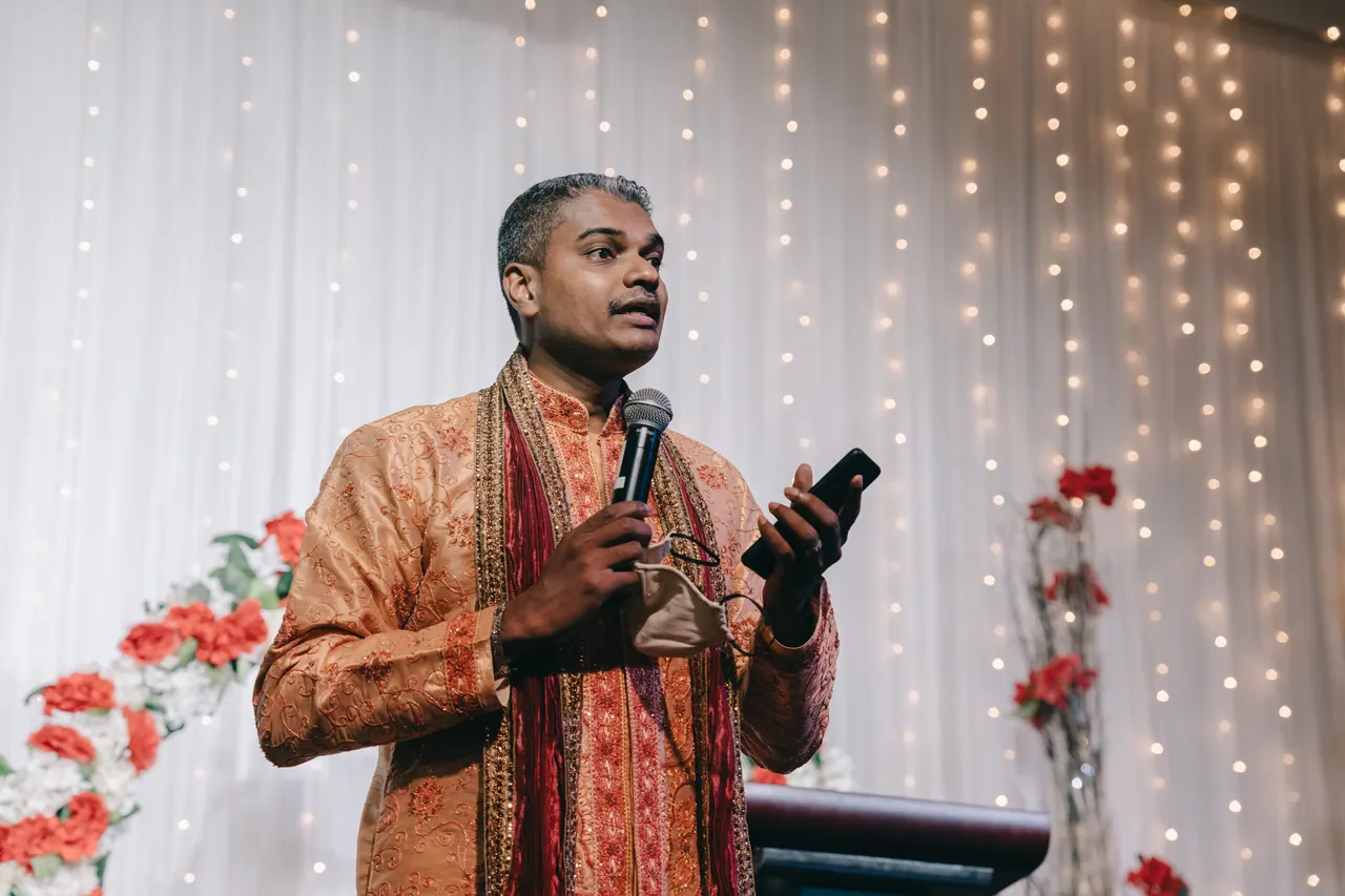 A man in an orange kurta speaks into a microphone.