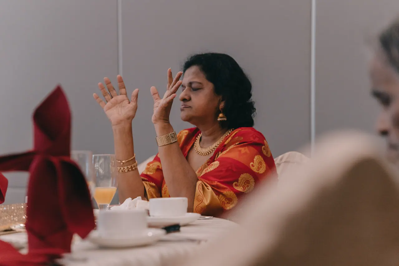 A woman in a red sari raises her hands, eyes closed.