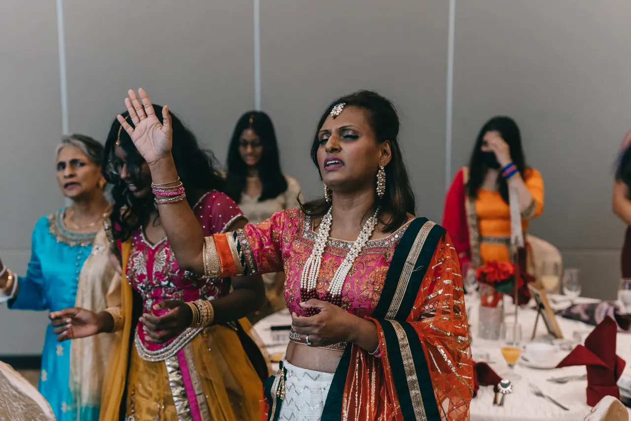Women in bright saris raise their hands in song.