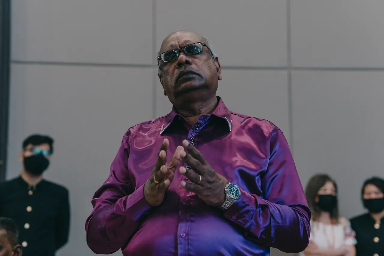 A man in purple prays with his hands together.