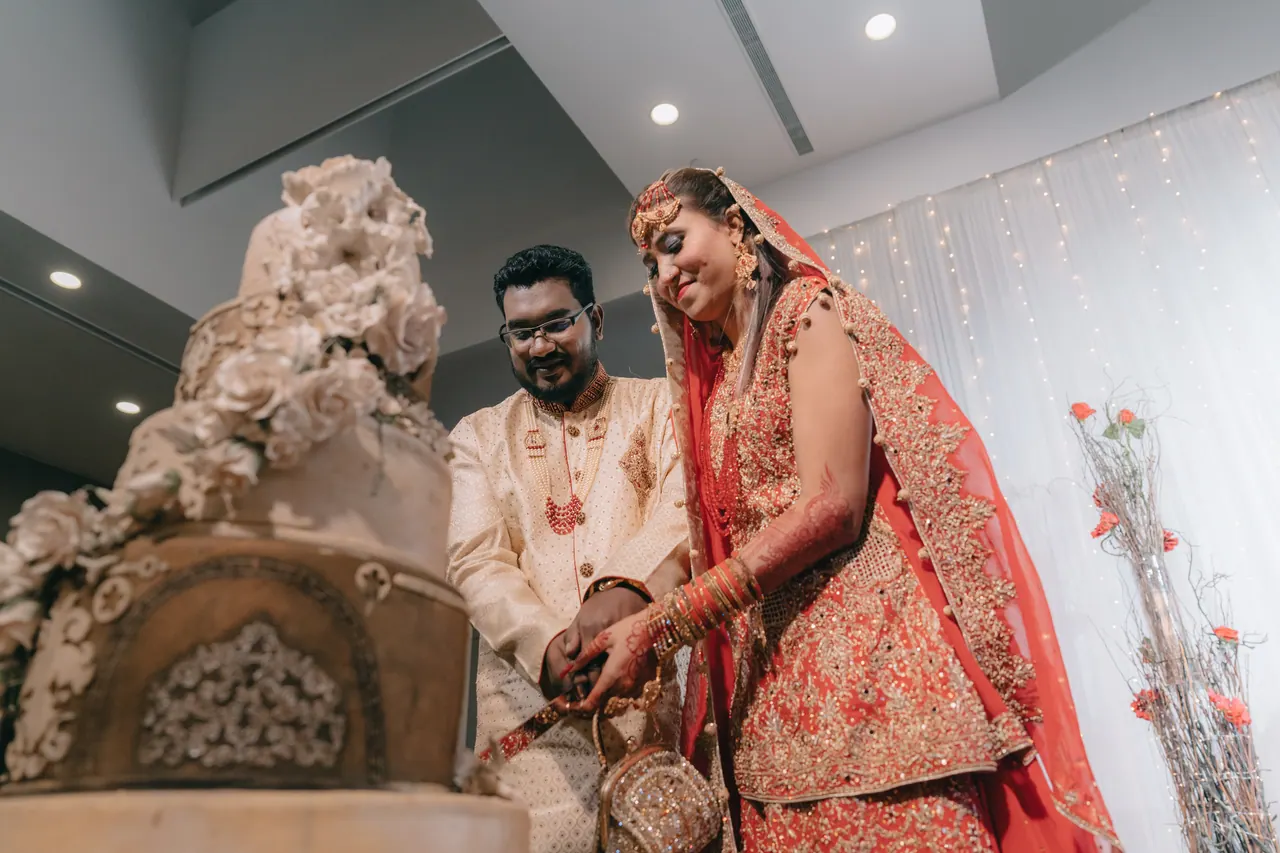 The couple in red and gold cut a tall white cake.