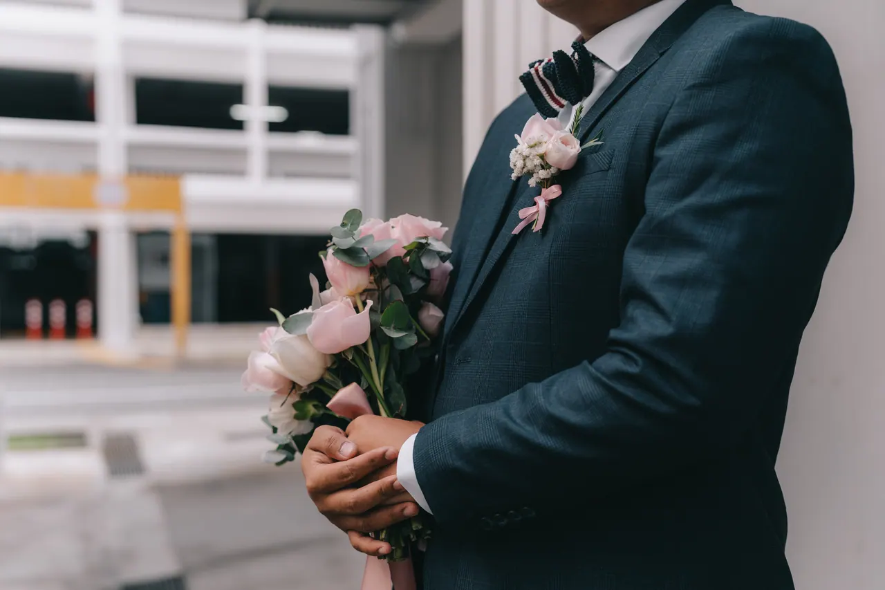 The groom holds a bouquet of pink roses against his navy suit.