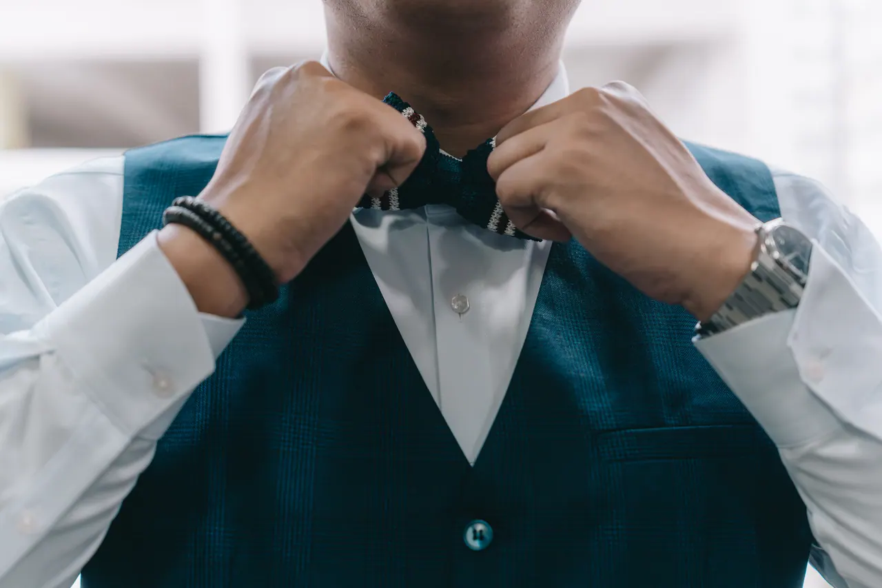 The groom straightens his bow tie, close up.