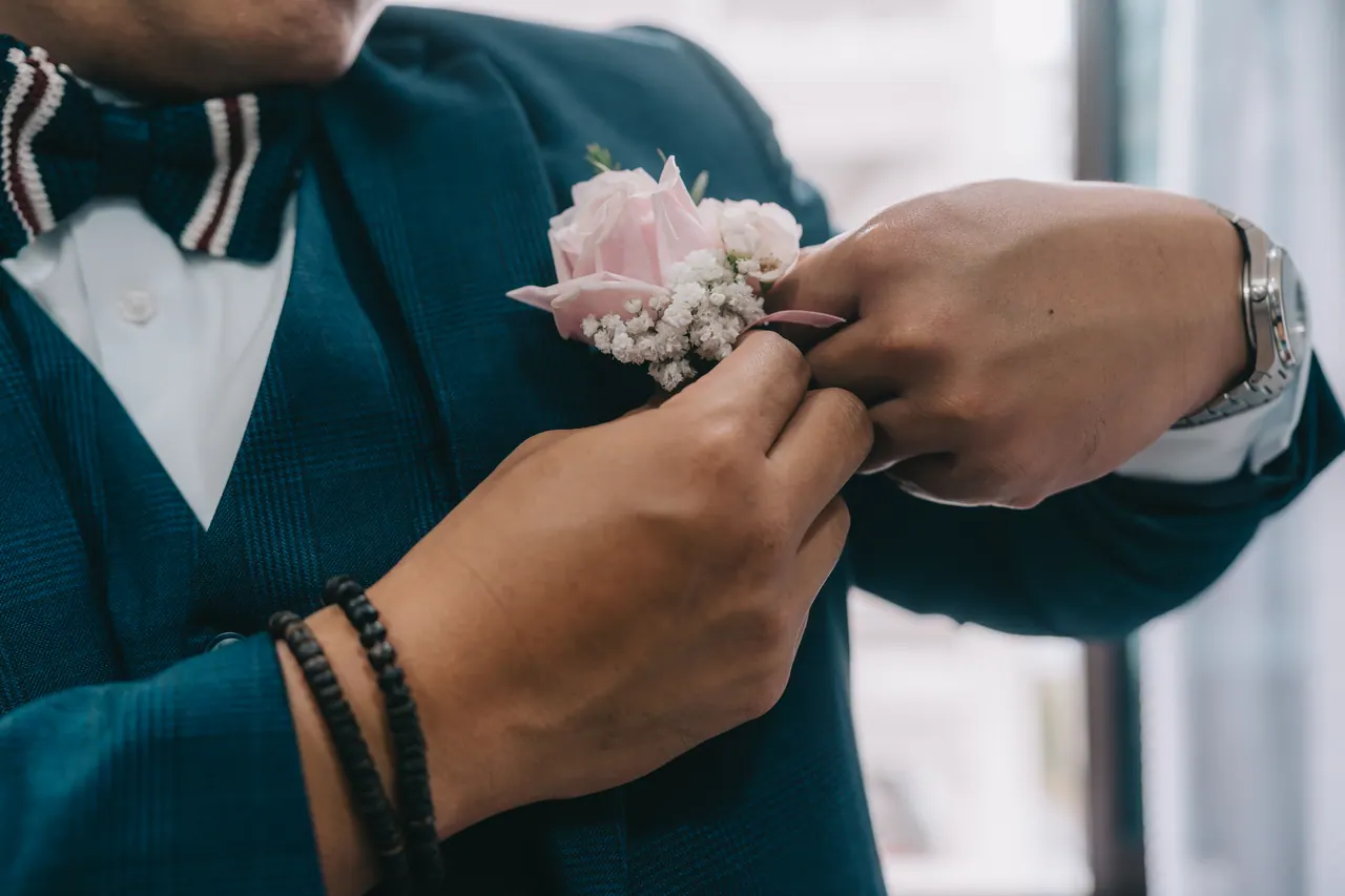 Hands pin a pink boutonniere to the groom’s lapel.