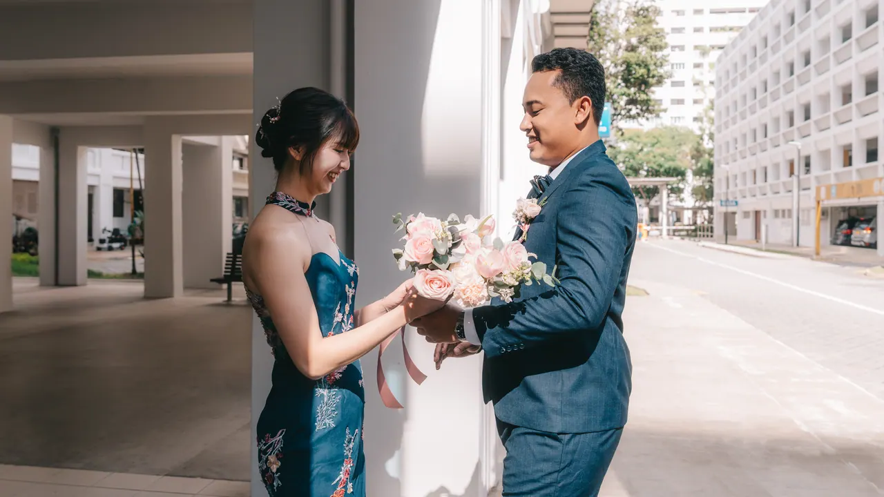 The bride and groom meet in a quiet street; he hands her the bouquet.