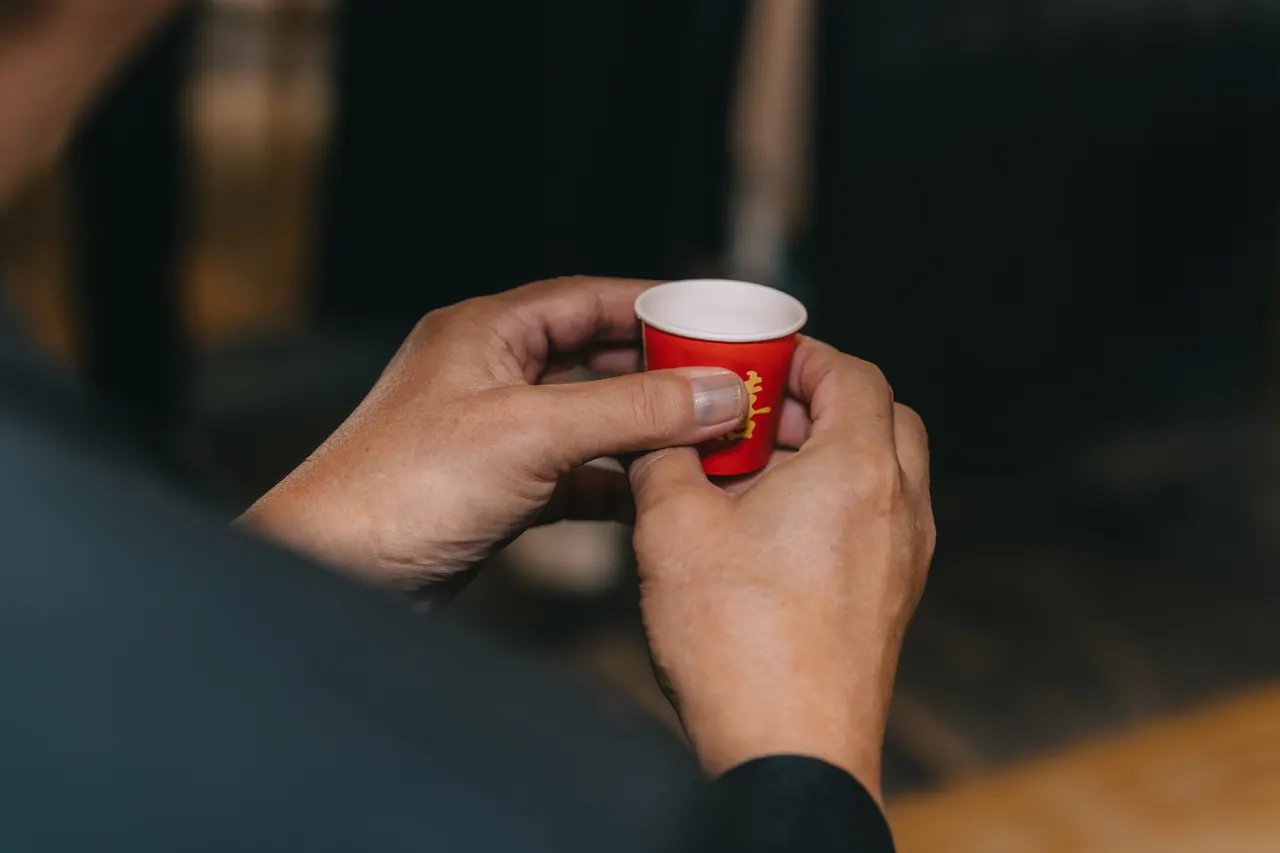 Hands hold a small red cup of tea.