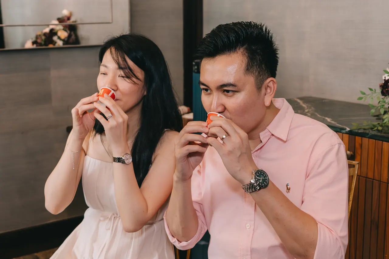 Two guests in pink and white sip from small red cups.