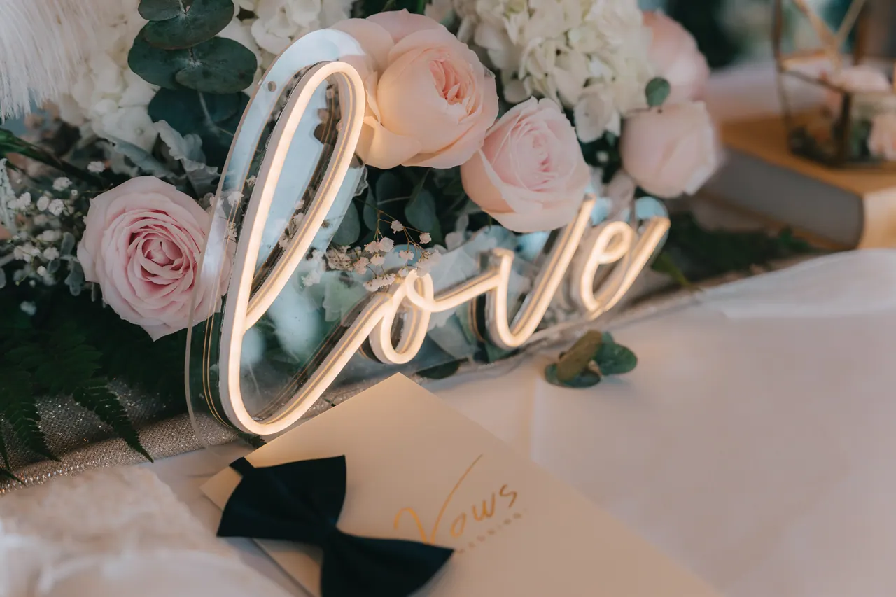 A neon sign reading love among pink roses.